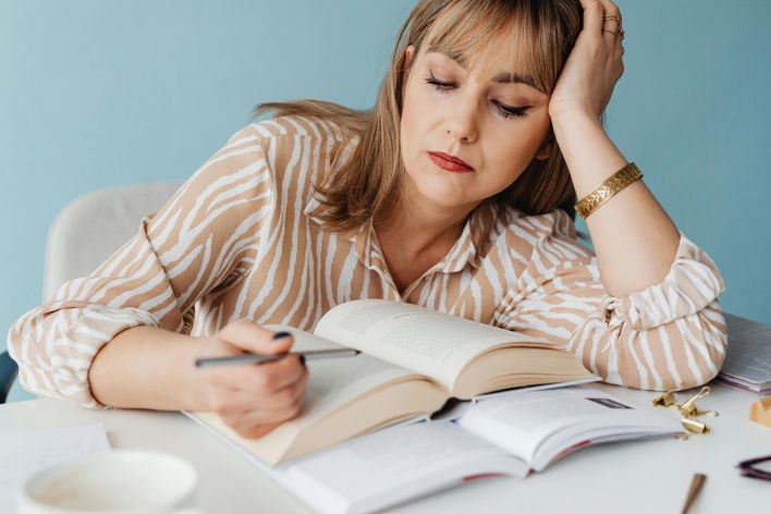 Exhausted woman resting her head on hand while reading a book at home.