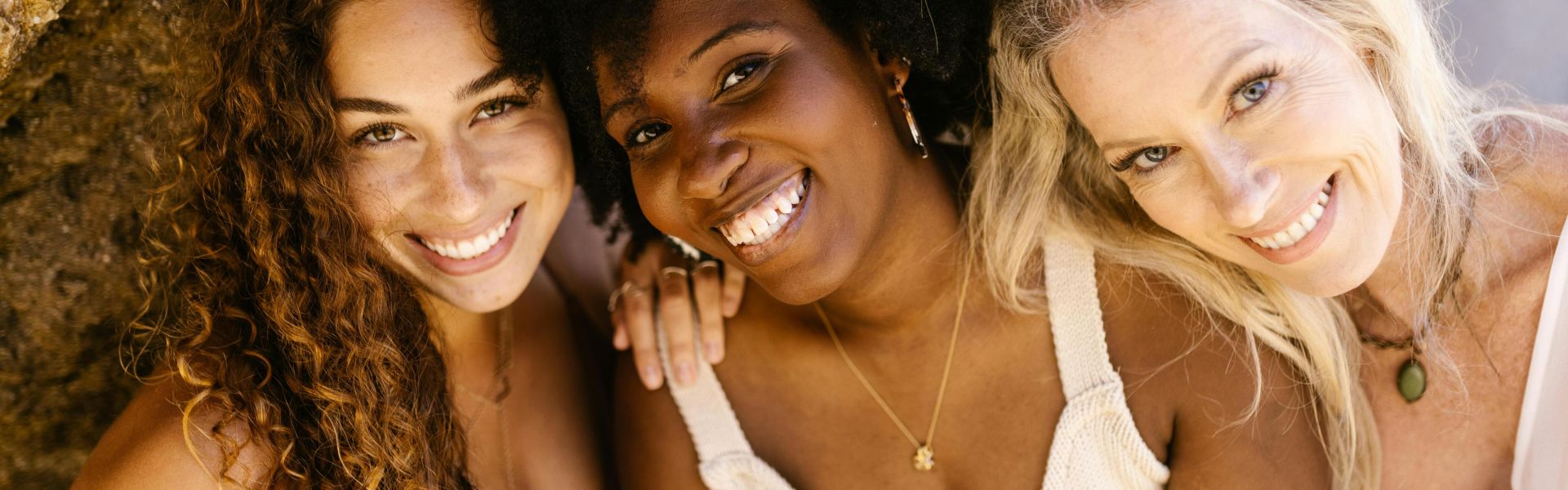 Three diverse women smiling warmly at the camera, celebrating friendship and diversity.