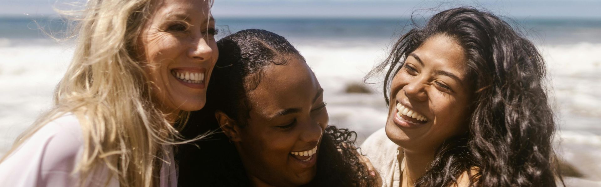Three women enjoying a sunny day at the beach, laughing and creating memories together.