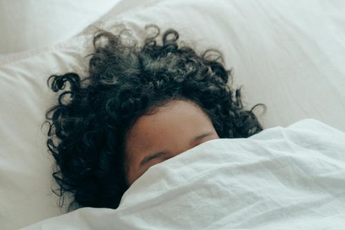 A person with curly hair sleeping peacefully under a white blanket, creating a sense of calm.