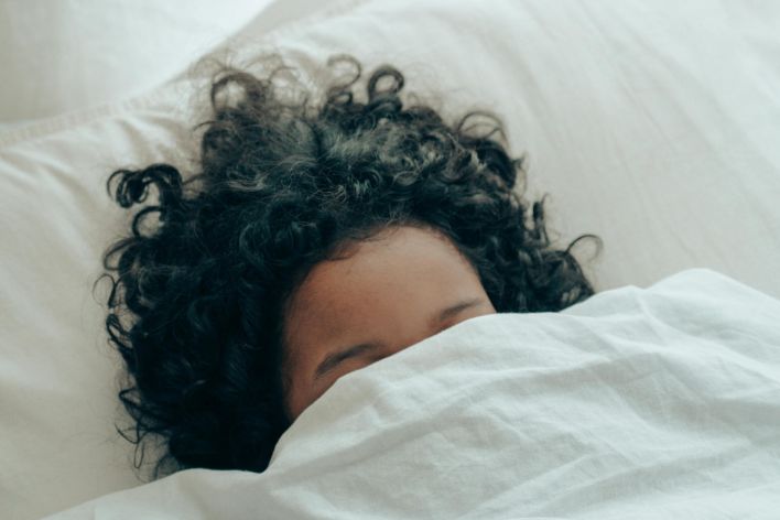 A person with curly hair sleeping peacefully under a white blanket, creating a sense of calm.
