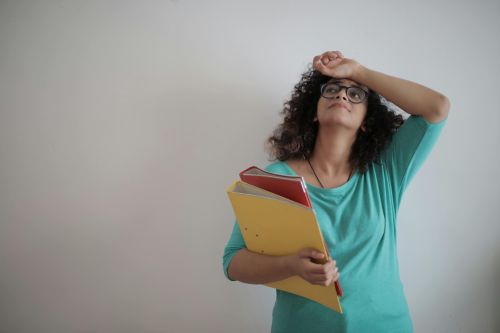 A woman in a teal top looks overwhelmed while holding colorful folders, symbolizing workplace stress.
